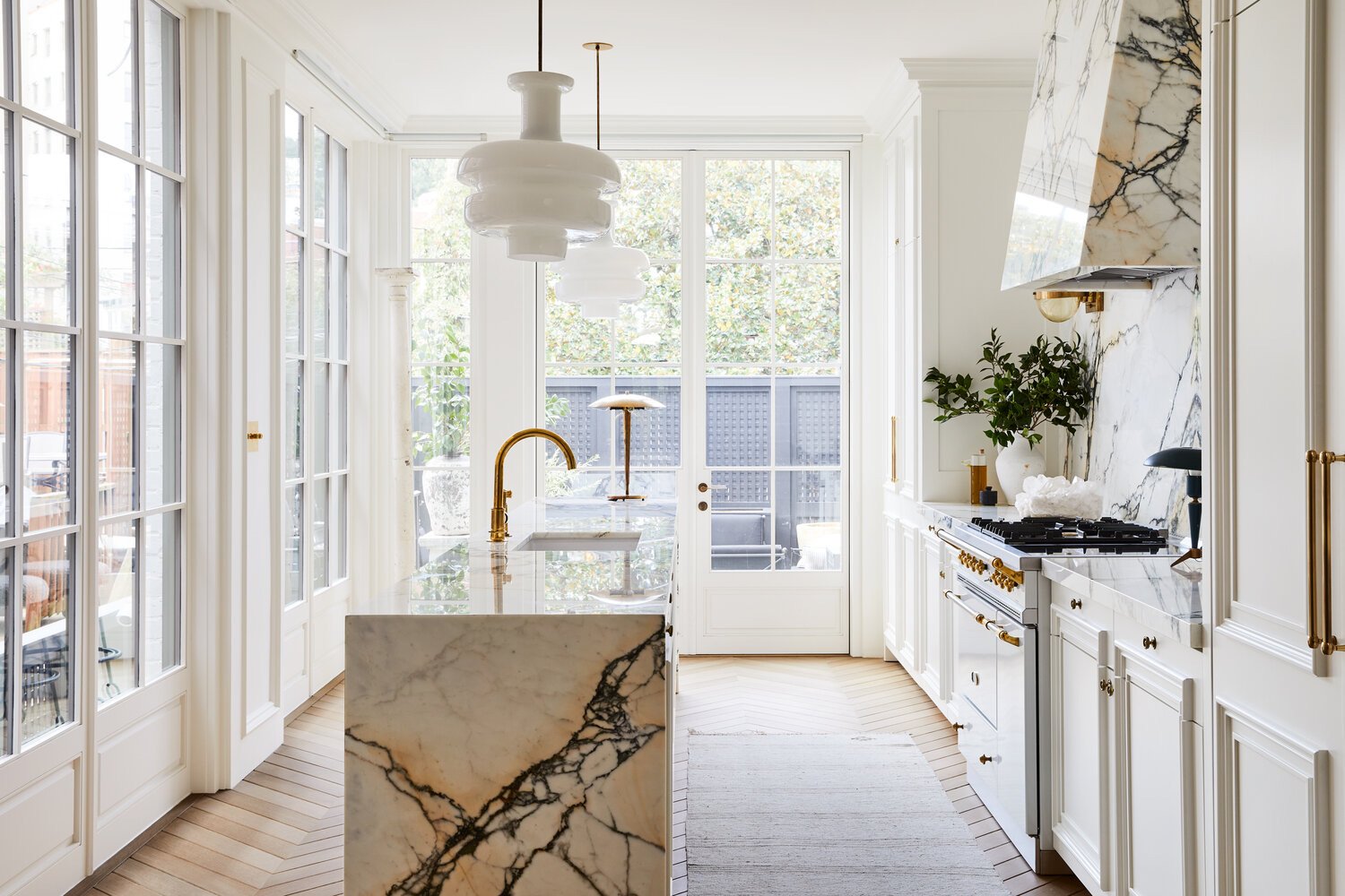 A bright marble kitchen with gold accents and a white chandelier